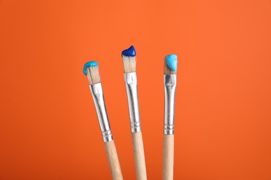 Photo of Three brushes with color paints on orange background, closeup