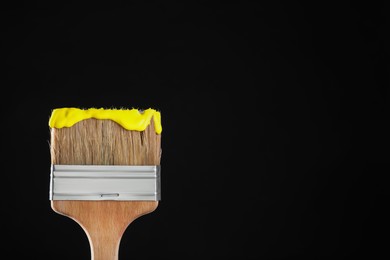 Photo of Brush with yellow paint on black background, closeup. Space for text