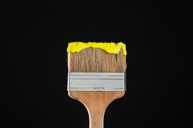 Photo of Brush with yellow paint on black background, closeup