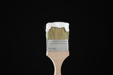 Photo of Brush with white paint on black background, closeup