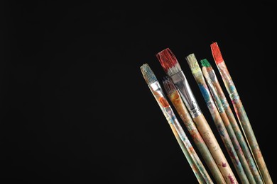 Photo of Many dirty paintbrushes on black background, closeup. Space for text