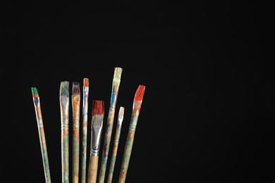 Photo of Many dirty paintbrushes on black background, closeup. Space for text