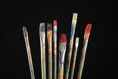 Photo of Many dirty paintbrushes on black background, closeup