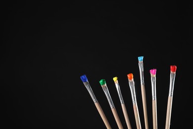 Photo of Many brushes with color paints on black background, closeup. Space for text