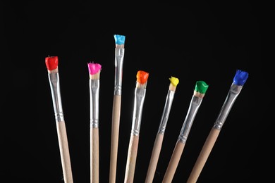Photo of Many brushes with color paints on black background, closeup