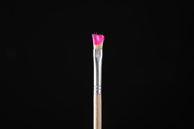 Photo of Brush with pink paint on black background, closeup