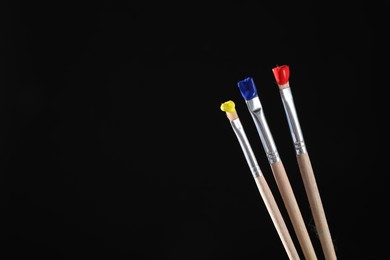 Photo of Three brushes with color paints on black background, closeup. Space for text