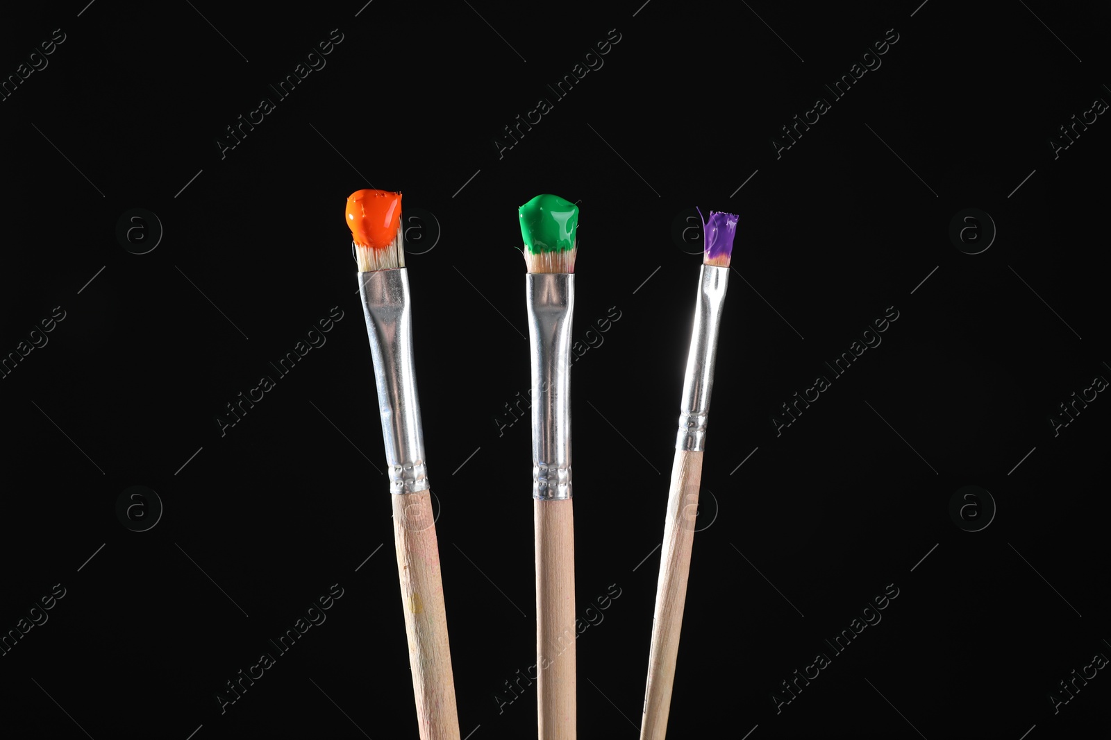 Three brushes with color paints on black background, closeup Photo of Three brushes with color paints on black background, closeup