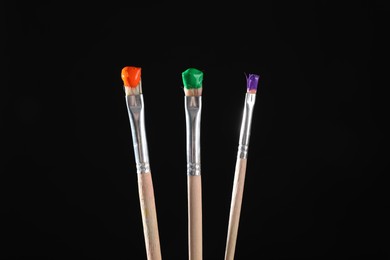 Photo of Three brushes with color paints on black background, closeup