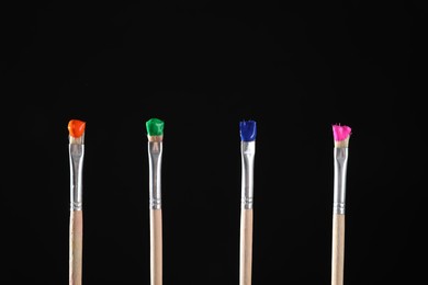 Photo of Many brushes with color paints on black background, closeup