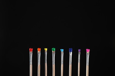 Photo of Many brushes with color paints on black background, closeup. Space for text