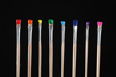 Photo of Many brushes with color paints on black background, closeup