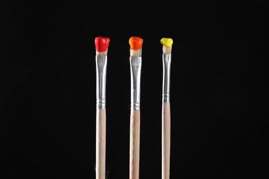 Photo of Three brushes with color paints on black background, closeup