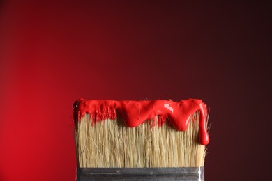 Photo of Brush with paint on red background, closeup. Space for text