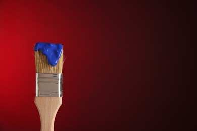 Photo of Brush with blue paint on red background, closeup. Space for text