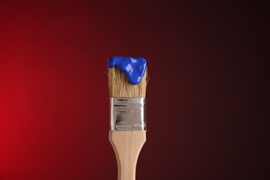 Photo of Brush with blue paint on red background, closeup