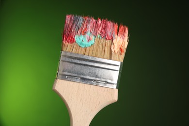 Photo of One dirty paintbrush on green background, closeup
