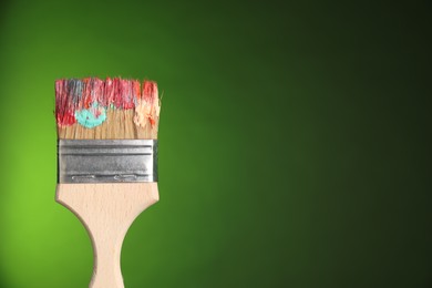 Photo of One dirty paintbrush on green background, closeup. Space for text