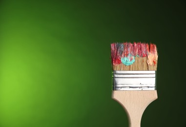Photo of One dirty paintbrush on green background, closeup. Space for text