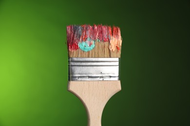 Photo of One dirty paintbrush on green background, closeup
