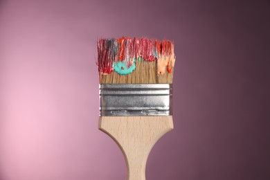 Photo of One dirty paintbrush on pink background, closeup