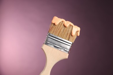 Photo of Brush with paint on pink background, closeup