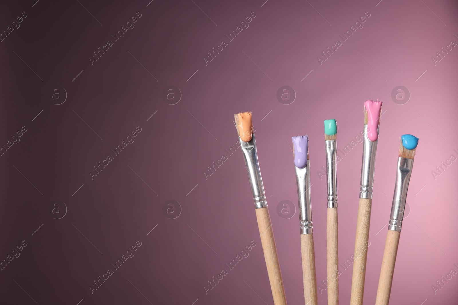 Many brushes with color paints on pink background, closeup. Space for text Photo of Many brushes with color paints on pink background, closeup. Space for text