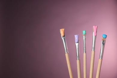 Photo of Many brushes with color paints on pink background, closeup. Space for text