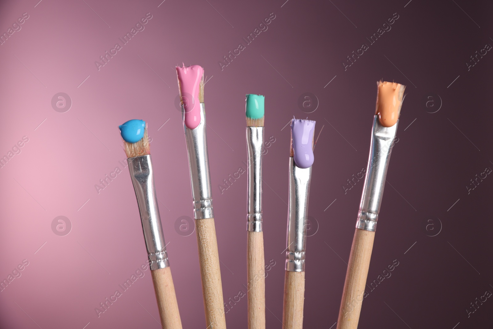 Many brushes with color paints on pink background, closeup Photo of Many brushes with color paints on pink background, closeup