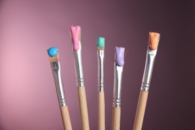 Photo of Many brushes with color paints on pink background, closeup