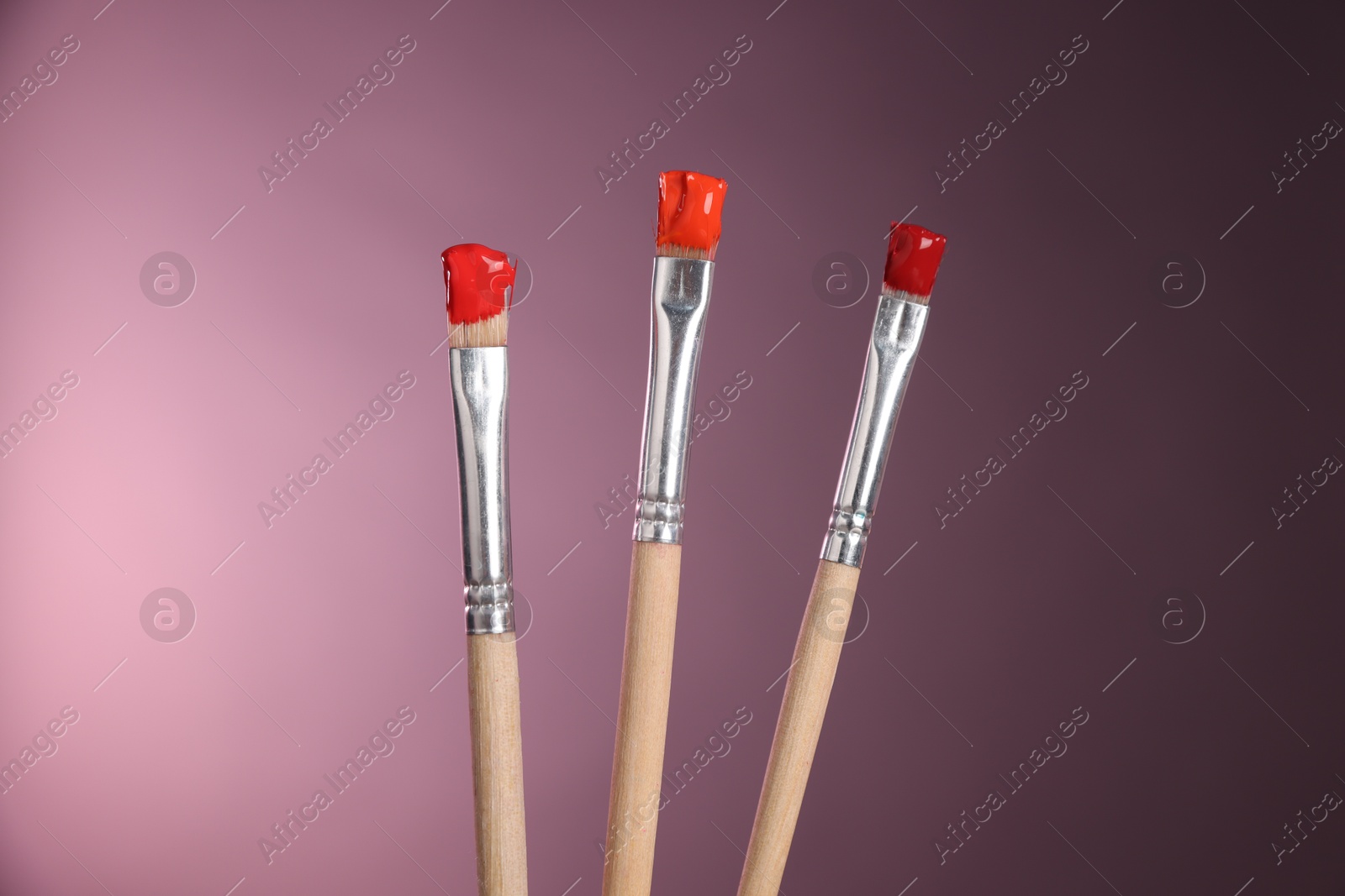 Three brushes with color paints on pink background, closeup Photo of Three brushes with color paints on pink background, closeup