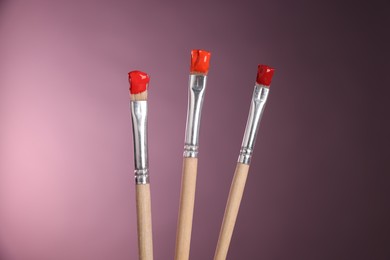 Photo of Three brushes with color paints on pink background, closeup