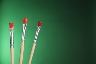 Photo of Three brushes with color paints on green background, closeup. Space for text
