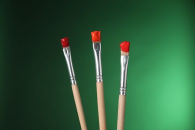 Photo of Three brushes with color paints on green background, closeup