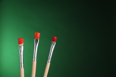 Photo of Three brushes with color paints on green background, closeup. Space for text
