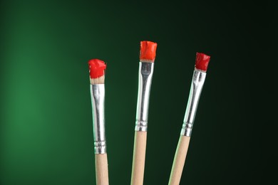 Photo of Three brushes with color paints on green background, closeup