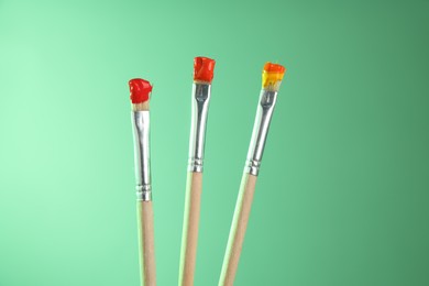 Photo of Three brushes with color paints on light green background, closeup