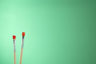 Photo of Two brushes with color paints on light green background, closeup. Space for text