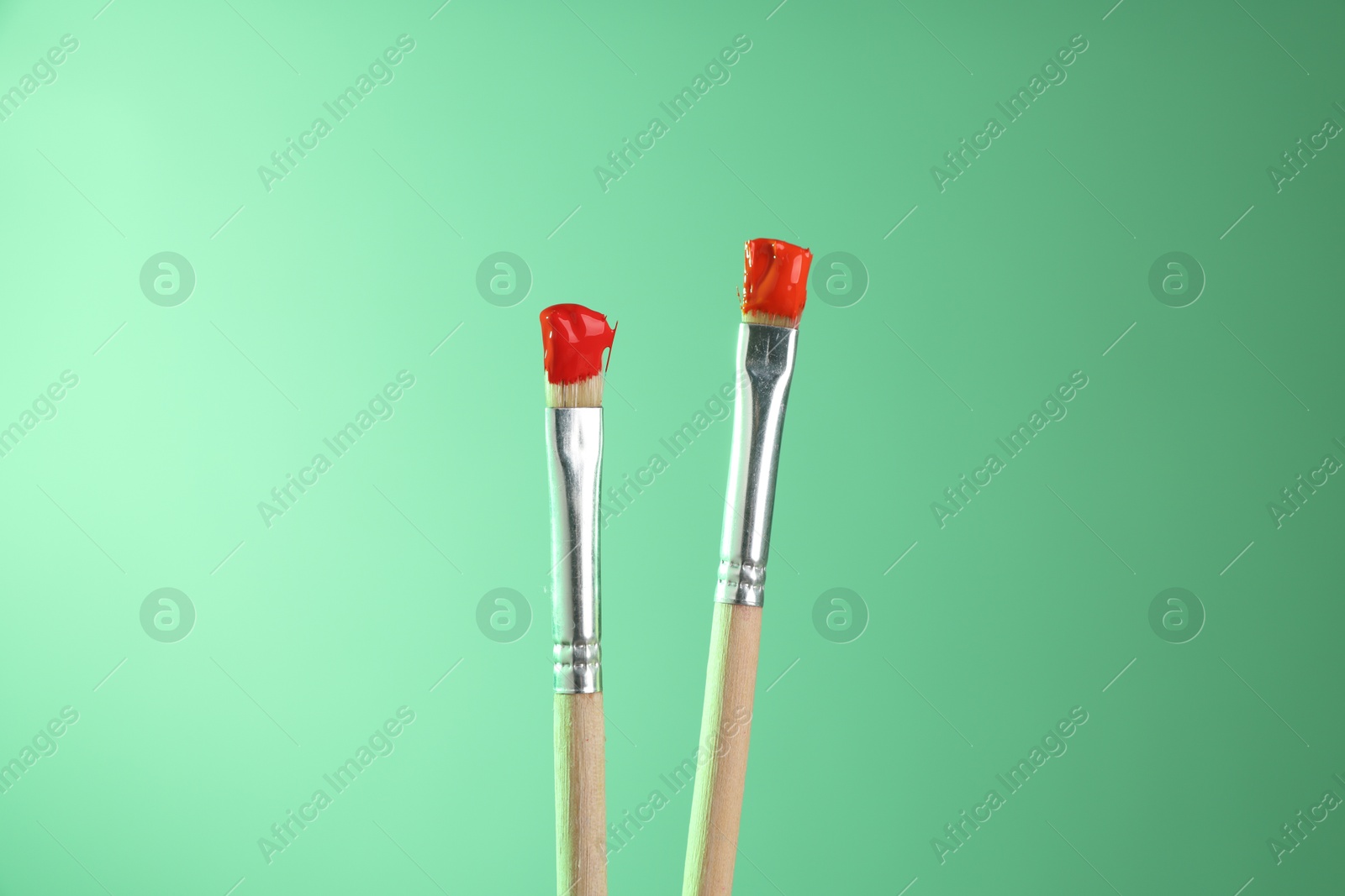 Two brushes with color paints on light green background, closeup Photo of Two brushes with color paints on light green background, closeup