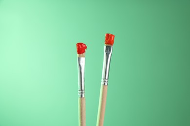Photo of Two brushes with color paints on light green background, closeup