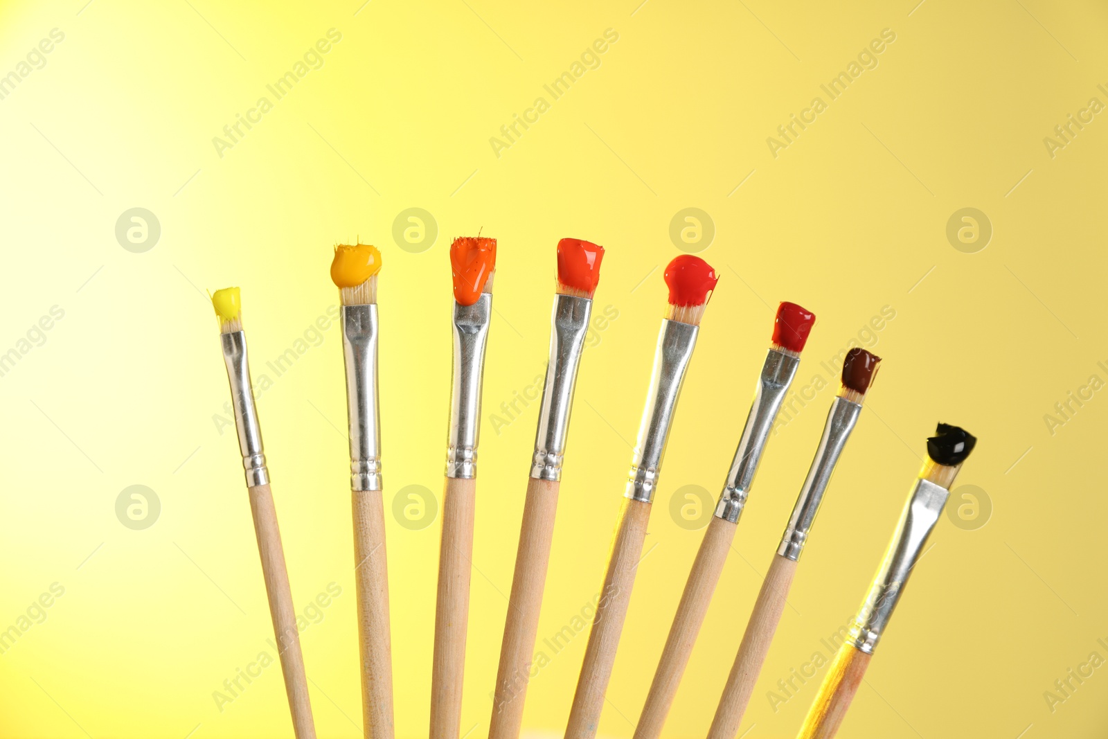 Many brushes with color paints on yellow background, closeup Photo of Many brushes with color paints on yellow background, closeup