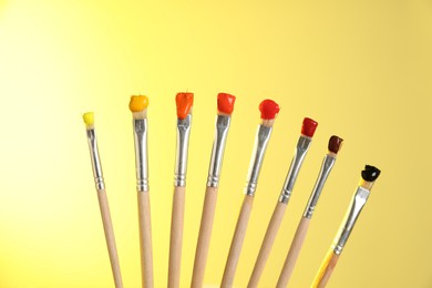 Photo of Many brushes with color paints on yellow background, closeup