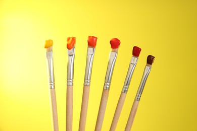 Photo of Many brushes with color paints on yellow background, closeup