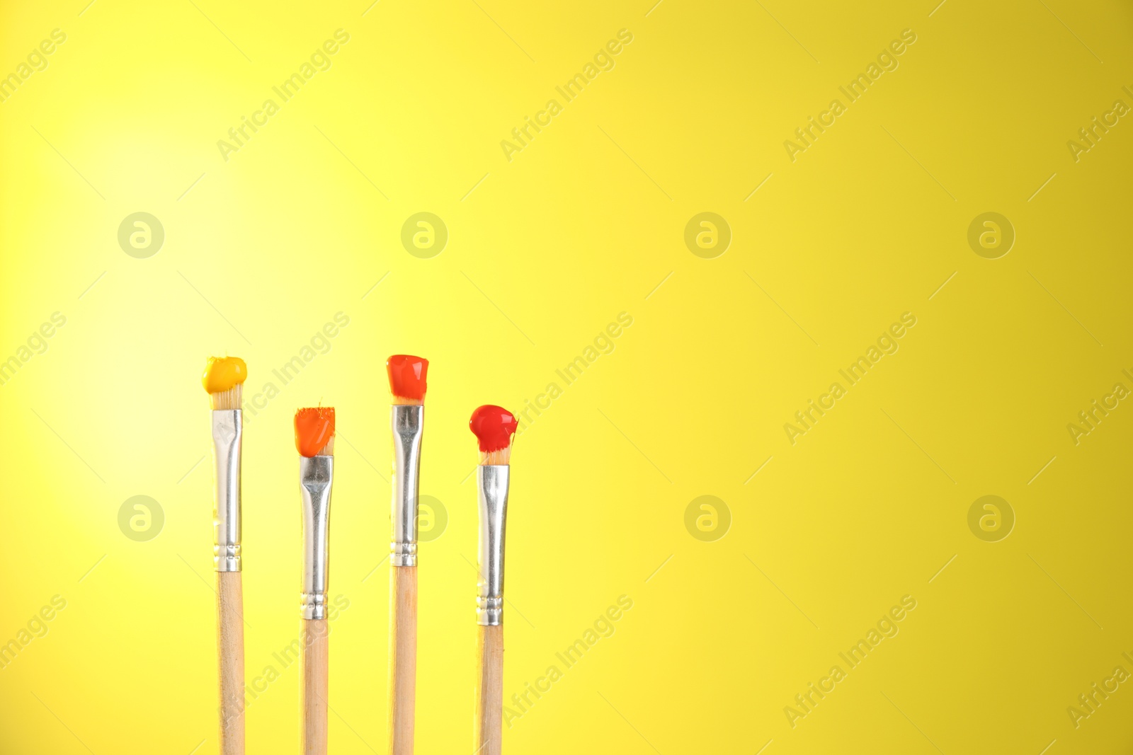Many brushes with color paints on yellow background, closeup. Space for text Photo of Many brushes with color paints on yellow background, closeup. Space for text