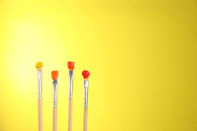 Photo of Many brushes with color paints on yellow background, closeup. Space for text