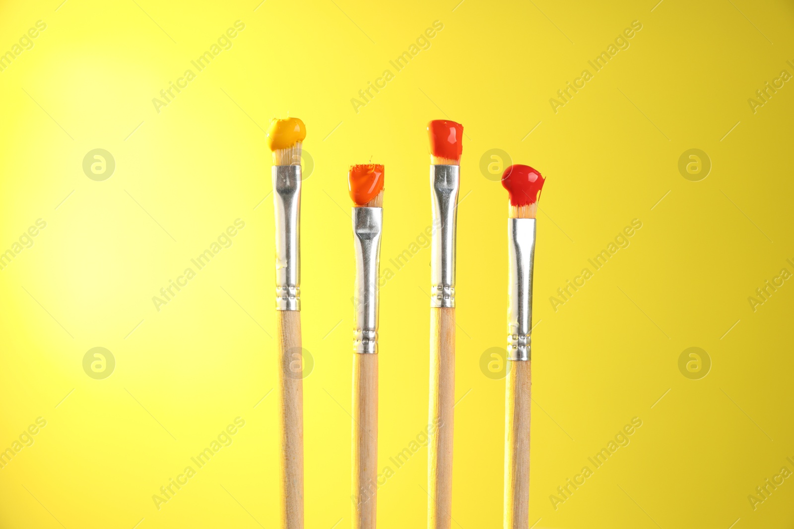 Many brushes with color paints on yellow background, closeup Photo of Many brushes with color paints on yellow background, closeup