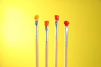 Photo of Many brushes with color paints on yellow background, closeup