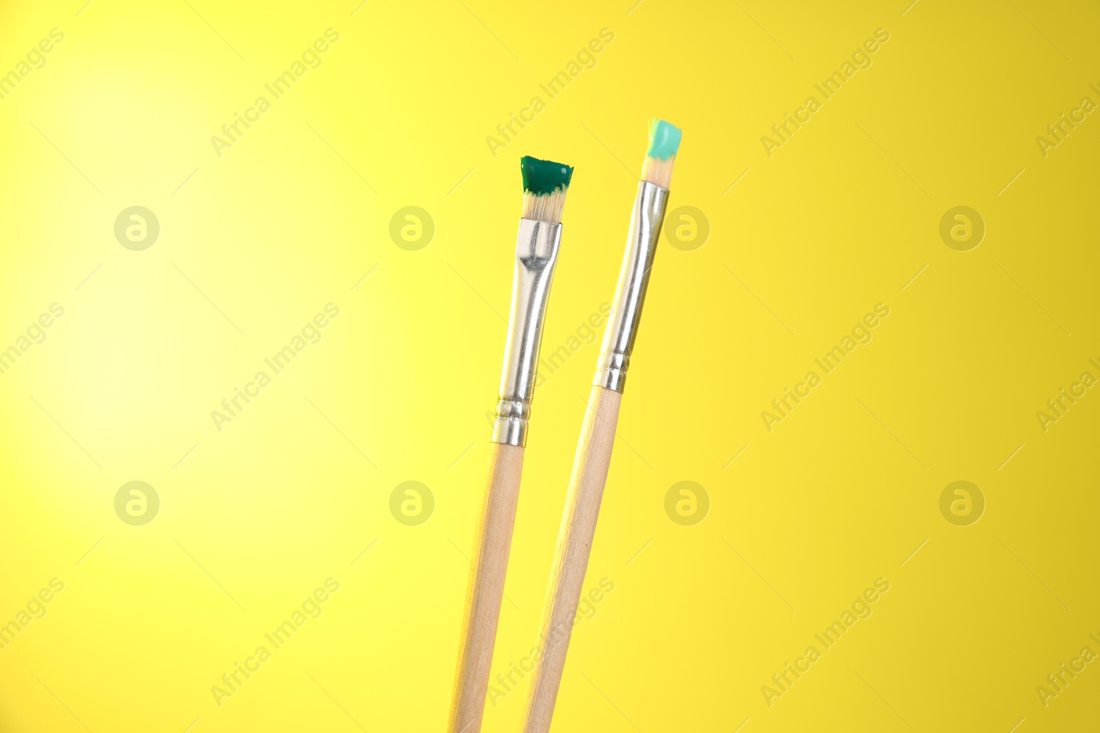 Two brushes with color paints on yellow background, closeup Photo of Two brushes with color paints on yellow background, closeup