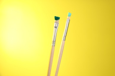 Photo of Two brushes with color paints on yellow background, closeup