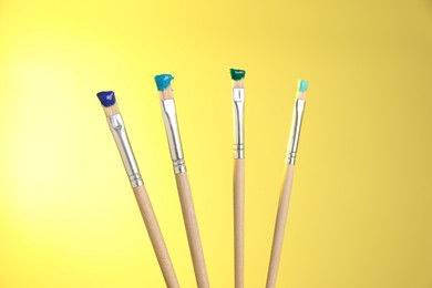 Photo of Many brushes with color paints on yellow background, closeup